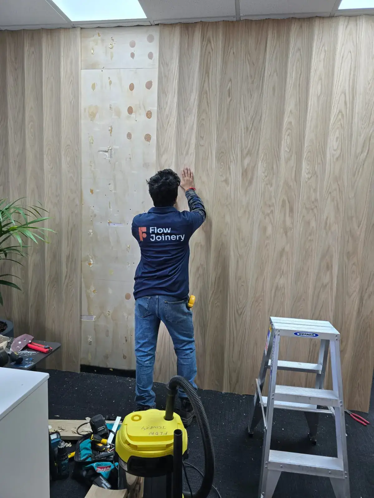 Flow Joinery team member fitting timber veneer wall panels in an office